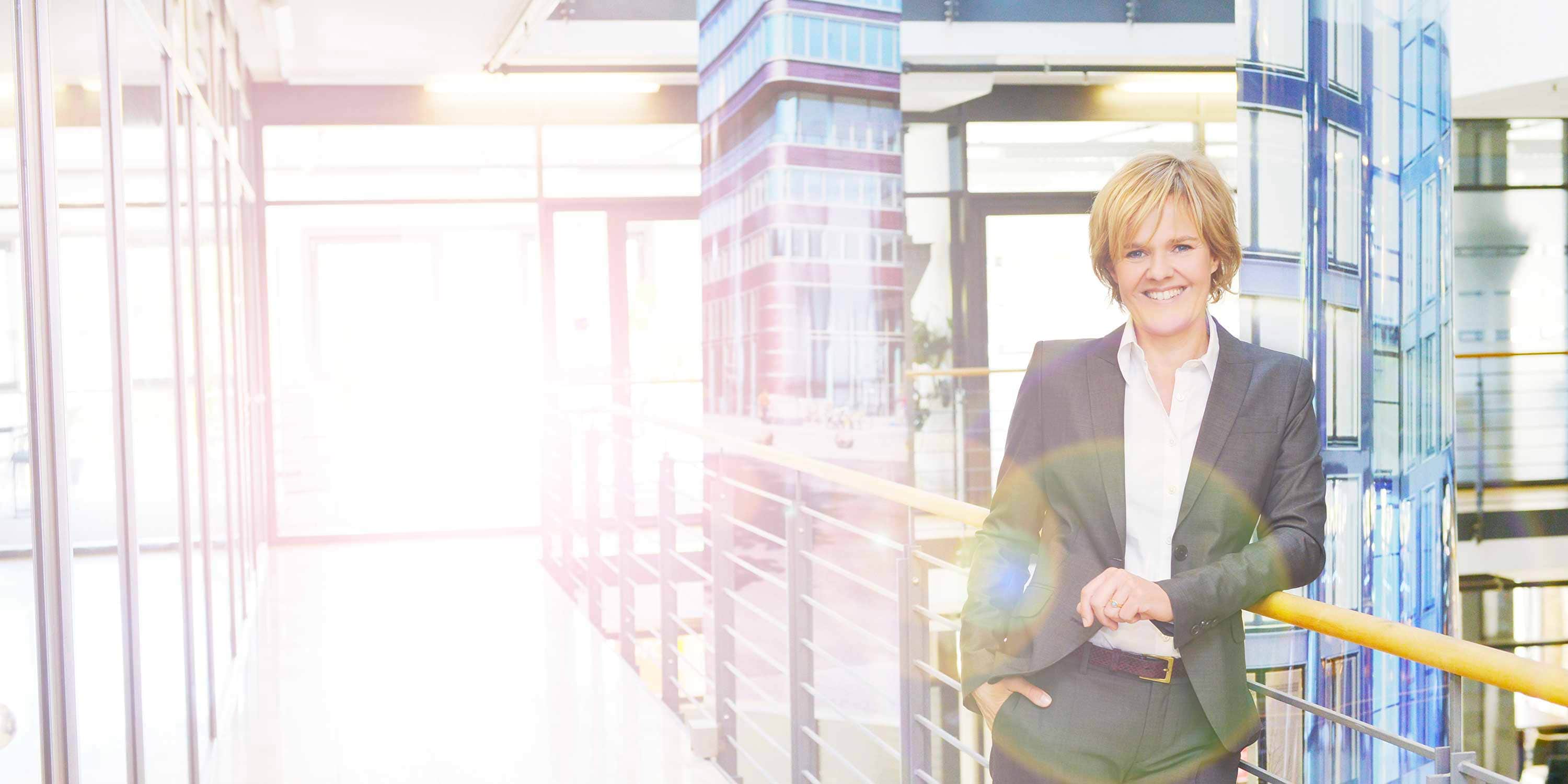 Ariane Ernst lehnt an einem Geländer in einem hellen, offenen Bürogebäude